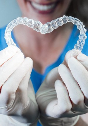 Invisalign dentist in Mount Pleasant holding two clear aligners in the shape of a heart 