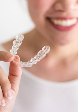 person smiling while holding an Invisalign aligner 