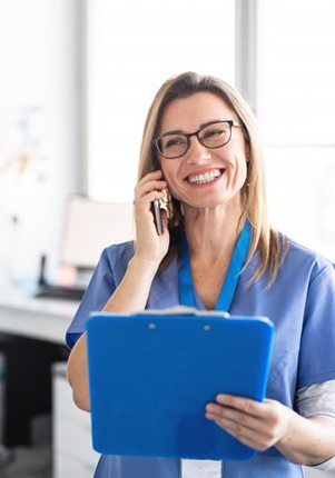 dental team member talking on the phone while holding a blue clipboard 