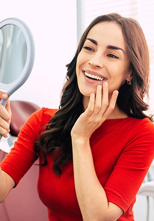Woman looking at smile in mirror after professional teeth whitening