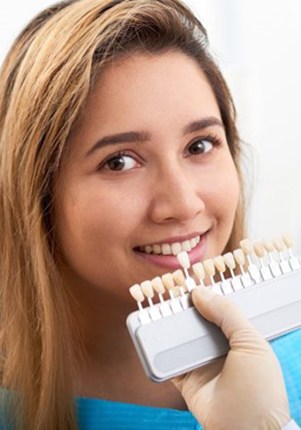 cosmetic dentist in Mount Pleasant holding a row of veneers up to a patient’s smile 