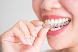 A smiling woman holding Invisalign clear braces