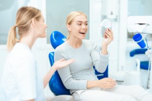 a woman smiling in the mirror with her cosmetic dentist by her side